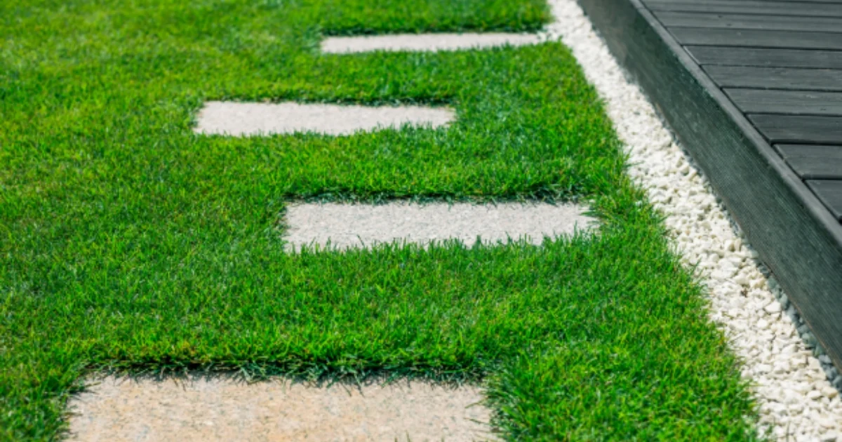Decorative stone path embedded in lush artificial grass with a border of white pebbles.